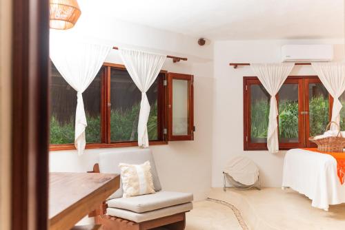 a living room with a table and a chair and windows at Casa Takywara in Holbox Island