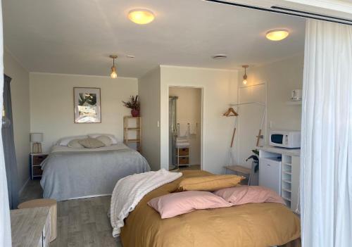 a bedroom with two beds and a kitchen with a microwave at Pāpāmoa Beach Studio Oasis in Papamoa