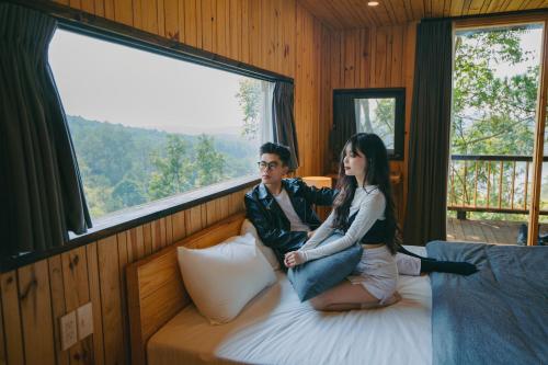 a man and woman sitting on a bed in a room with a window at Lavender Dalat Hotel and Resorts in Da Lat