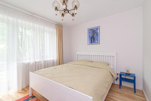 a white bedroom with a bed and a chandelier at Slow-down, relax, take it easy in artsy Oasy in Vilnius