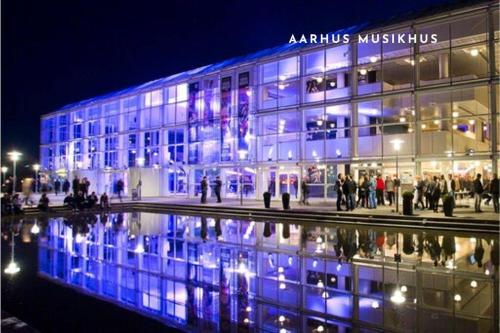 a building with a reflection in the water at night at Bo med stil og udsigt til Aarhus lystbådehavn in Aarhus