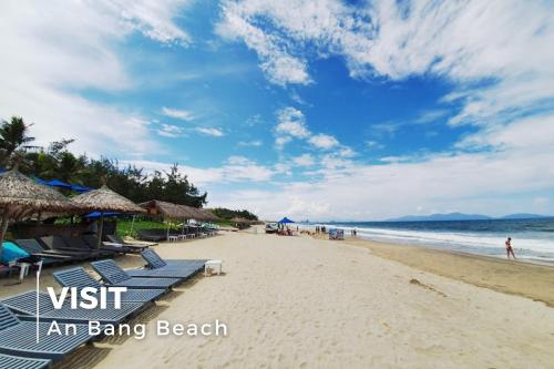 an empty beach with chairs and umbrellas and the ocean at La Charm Hoi An Hotel & Spa in Hoi An