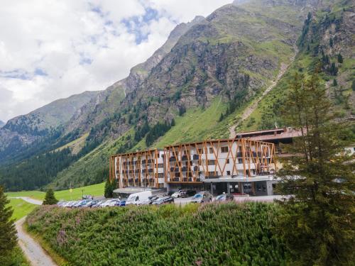 a building with cars parked in front of a mountain at Hotel Gundolf in Sankt Leonhard im Pitztal