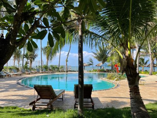 una piscina con 2 sillas y palmeras en MUINE SUN AND SEA RESORT & GLAMPING, en Mui Ne