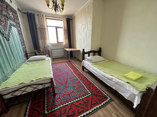 a room with two beds and a rug and a window at Kurak Homestay in Bishkek