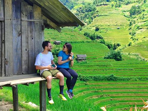 a man and woman sitting on a bench in front of a field at Mu Cang Chai Homestay & Trekking in Mù Cang Chải
