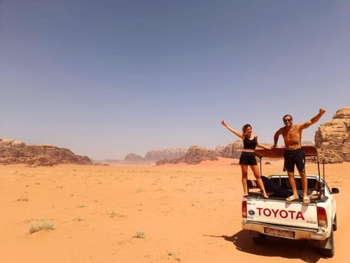 two people standing on the back of a truck in the desert at Desert Nights Camp in Wadi Rum