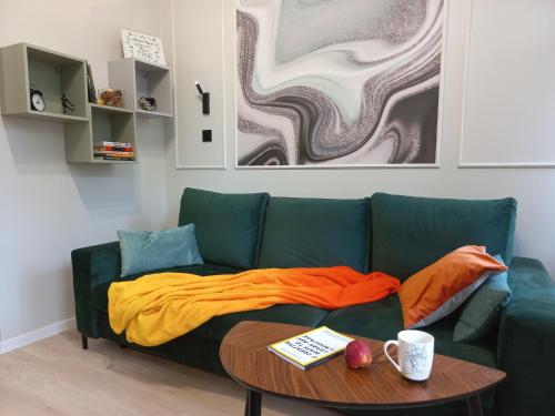 um sofá verde com um cobertor laranja e uma mesa em Przytulne studio przy Atlas Arena i malowniczym parku em Lódź