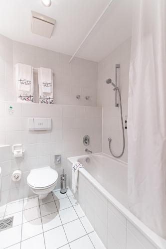 a white bathroom with a toilet and a bath tub at Taste Hotel Kulmbach in Kulmbach