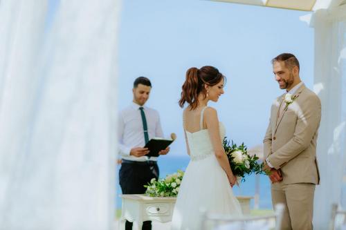 a bride and groom standing in front of a priest at Louis Ledra Beach in Paphos City