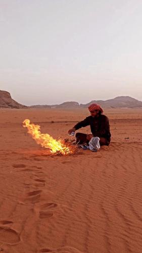 un hombre sentado en el desierto con un fuego en Wadi Rum Nature Stars Camp en Wadi Rum