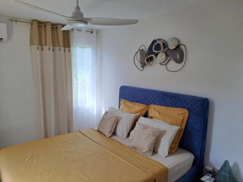 a bedroom with a blue bed with pillows and a ceiling fan at RDC appartement en bord de mer au son des vagues in Le Moule