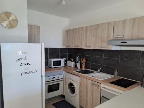 a kitchen with a white refrigerator and a sink at RDC appartement en bord de mer au son des vagues in Le Moule