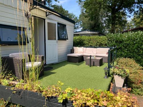 einen Hinterhof mit grünem Rasen mit Sofa und Stühlen in der Unterkunft Charmant chalet op een bospark op de Veluwe in Putten