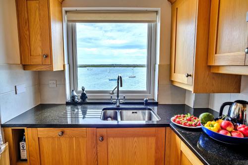 a kitchen with a sink and a window and a bowl of fruit at Finest Retreats - Kings Wharf - Luxury Riverside Home in Burnham-on-Crouch