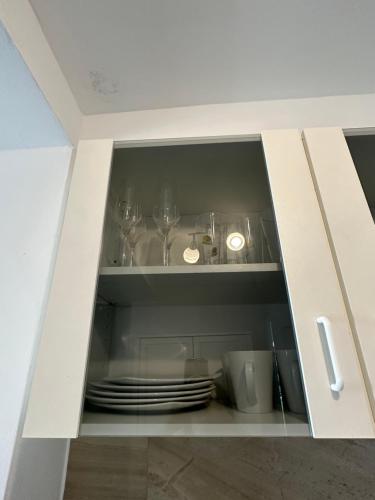 un armario blanco con platos y vasos. en Studio on the beach en Preko