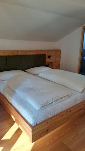 a bed with white sheets and a wooden headboard at Haus am Park in Rasùn di Sotto