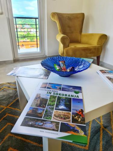 a table with a magazine on it with a chair at Apartman Berlin Sokobanja in Soko Banja
