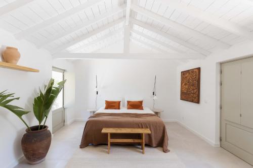 a white bedroom with a bed and a table at Âmago Guesthouse in Santa Bárbara de Nexe