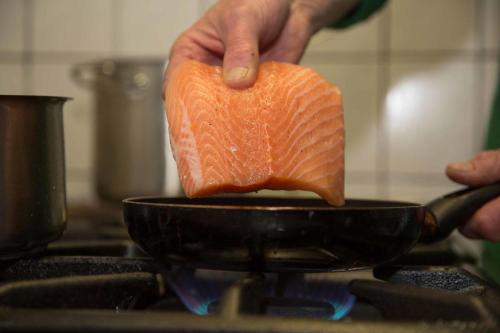 a person holding a piece of salmon in a pan at Hotel Klostermühle Siebenborn in Maring-Noviand