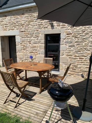 a wooden table and chairs with a grill and an umbrella at Les écuries du Nevez in Plonéour-Lanvern
