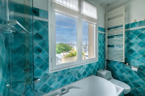 La salle de bains est pourvue de carrelage bleu, de toilettes et d'une fenêtre. dans l'établissement Veeve - A Romance in Rouge, à Paris