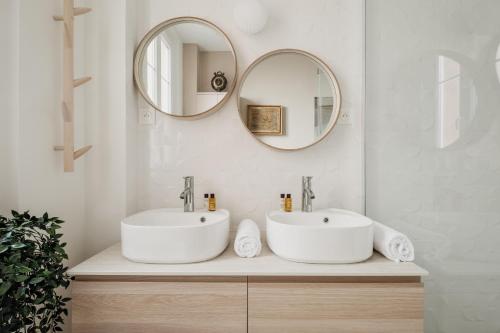 une salle de bain avec deux lavabos et deux miroirs dans l'établissement Veeve - La Vie Est Belle, à Paris