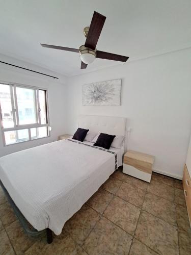 a white bedroom with a bed and a ceiling fan at Apartamento 50mt Playa Cullera (San Antonio) in Cullera