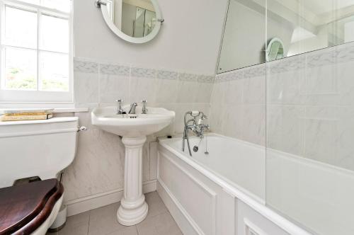 a white bathroom with a sink and a tub and a toilet at Veeve - Mews & Blues in London