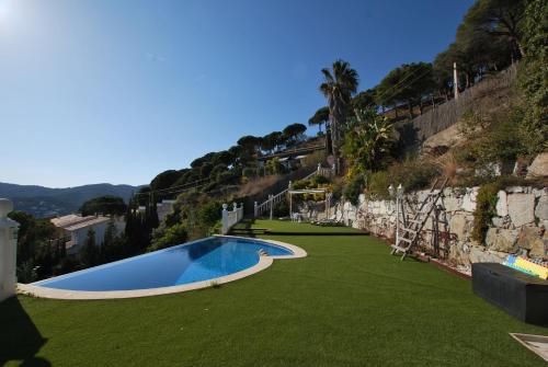 a swimming pool with green grass next to a wall at Sunny house in Cabrils