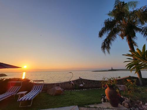 a sunset over the ocean with two chairs and a palm tree at Villas Jardin Del Mar in Cruz de Huanacaxtle