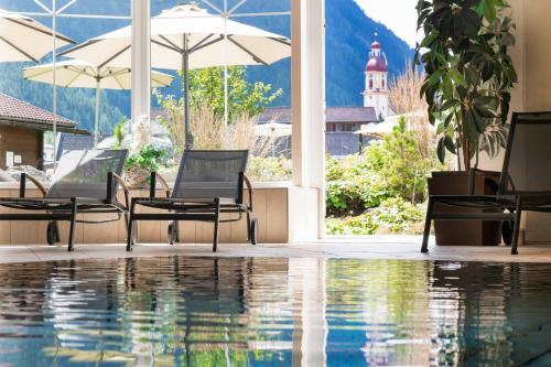 einem Pool mit Stühlen und einem Sonnenschirm und einem Gebäude in der Unterkunft Hotel Stubaierhof in Neustift im Stubaital