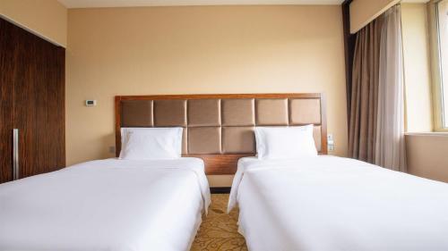 two beds in a hotel room with white sheets at Holiday Inn Mudanjiang by IHG in Mudanjiang