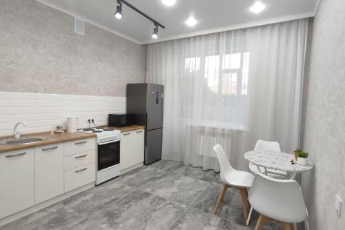 パヴロダルにあるЛюкс апартаменты в ЖК Shanyrakの白いキャビネット、テーブルと椅子付きのキッチンが備わります。