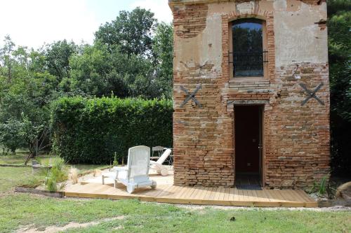 un bâtiment en briques avec une chaise sur une terrasse en bois dans l'établissement Le Biaou, à Albias