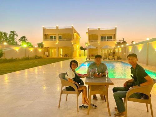 tres personas sentadas en una mesa frente a una casa en Royal Nile Villas - Nile View Apartment 1, en Luxor