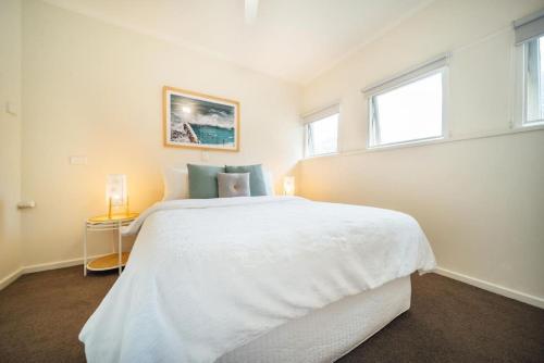 a white bedroom with a large bed and two windows at Beachy Keen on Moseley in Glenelg