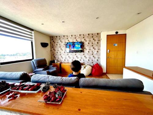 um rapaz sentado num sofá numa sala de estar em PENTHOUSE de lujo en las animas! A 5 minutos de plaza Angelópolis em El Gallinero