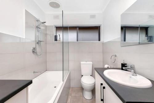 a white bathroom with a toilet and a sink at Moments on Moseley Glenelg in Glenelg
