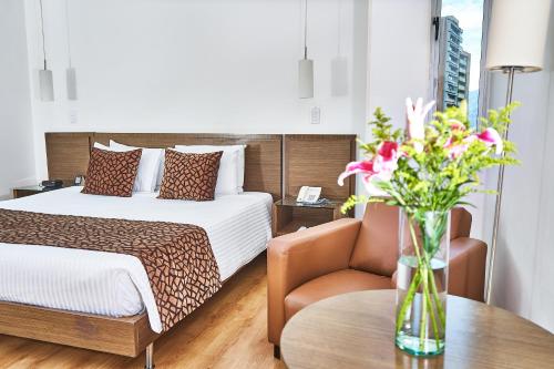 una habitación de hotel con una cama y un jarrón de flores sobre una mesa en Hotel Poblado Alejandria, en Medellín