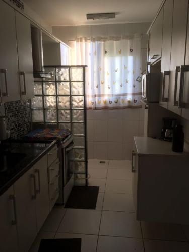 a kitchen with white cabinets and a window with a microwave at Apartamento ao lado Shopping in Campos dos Goytacazes