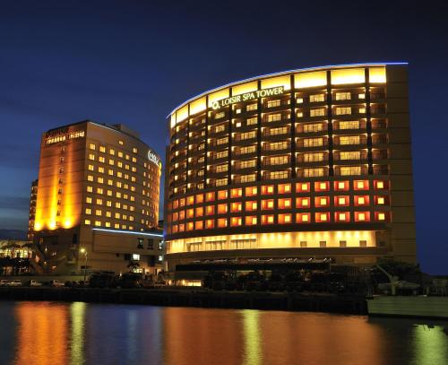 un bâtiment d'hôtel éclairé à côté d'une masse d'eau dans l'établissement Loisir Spa Tower Naha, à Naha