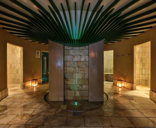 eine Lobby mit einer Steinsäule und einer grünen Decke in der Unterkunft TH Madonna di Campiglio | Golf Hotel in Madonna di Campiglio
