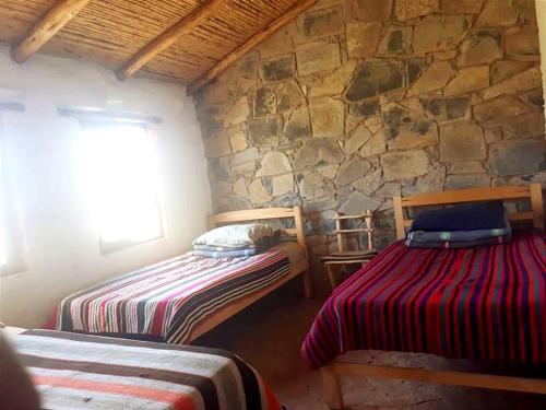 a bedroom with two beds and a stone wall at Samary -wasi maragua in Estancia Chaunaca