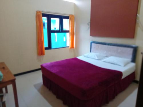 a bedroom with a bed with purple sheets and a window at Ijen Transito 2 HOMESTAY in Ketapang