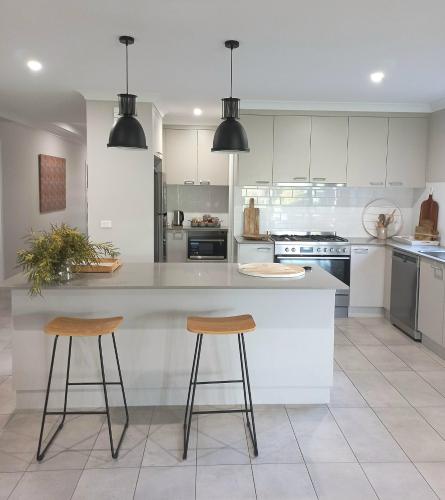 a kitchen with white cabinets and two bar stools at Kennedy House Euroa PERFECT FOR SHORT TERM STAYS in Euroa