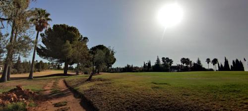 a golf course with palm trees and the sun in the sky at El Patio de las Minas in Aznalcázar