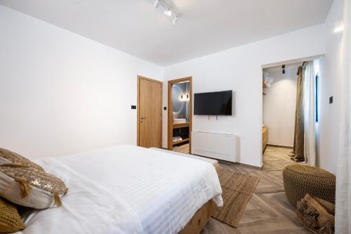 a white bedroom with a bed and a tv at RASTONI VILLAS BY AEGEAN HOUSES in Psalidi