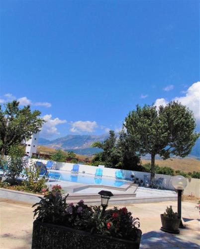 a swimming pool with chairs and flowers in a park at Hotel Mondo in Gjirokastër