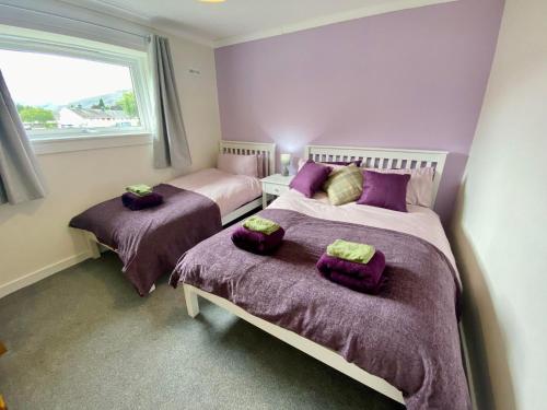 a bedroom with two beds with purple sheets and a window at cosy town bungalow in Inverlochy